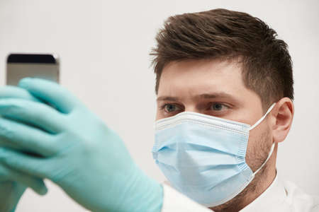 coronavirus concept a man in a medical mask looks at the phone in on a white backgroundの写真素材