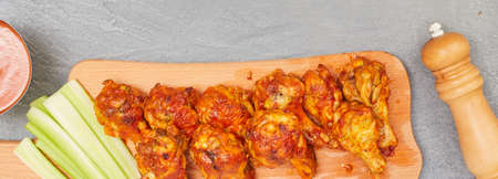 Buffalo chicken wings on a wooden board with celery on a concrete background, top view, copy spaceの写真素材