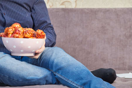 man on the couch with a plate of Buffalo Chicken Wings, copy spaceの写真素材