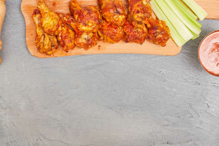 Buffalo chicken wings on a wooden board with celery on a concrete background, top view, copy spaceの写真素材