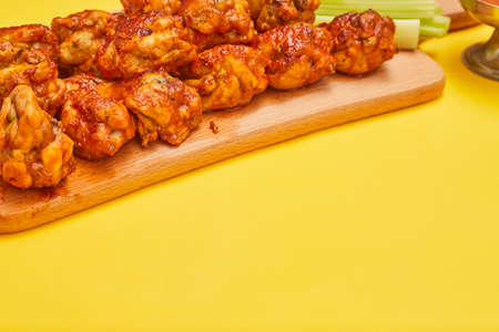 Buffalo chicken wings on a wooden board with celery on a yellow background, copy spaceの写真素材