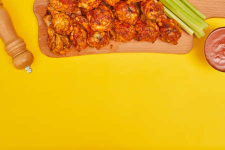 Buffalo chicken wings on a wooden board with celery on a yellow background, copy spaceの写真素材