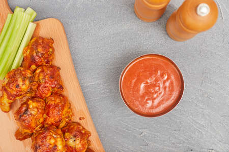 Buffalo chicken wings on a wooden board with celery on a concrete background, top view, copy spaceの写真素材