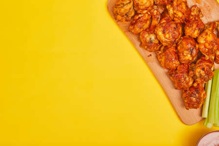 Buffalo chicken wings on a wooden board with celery on a yellow background, copy spaceの写真素材