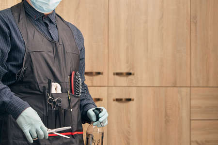 hairdresser, barber in an apron with gloves and a medical mask on a light backgroundの写真素材