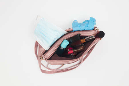 womens handbag with cosmetics and medical mask sanitizer, covid-19, flat lay