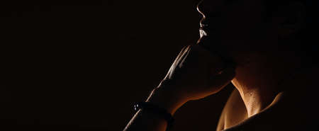 Caucasian man with a bared torso sits thoughtfully on a dark background, banner, in a dark key, close-upの写真素材