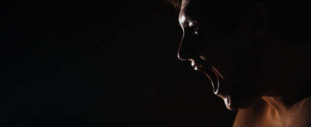 Caucasian man with a bared torso shouts on a dark background, banner, in a dark key, close-upの写真素材