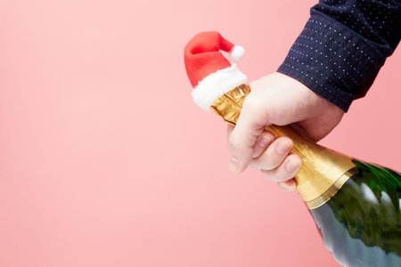 hand holds a bottle of champagne with santa hat on pink backgroundの写真素材