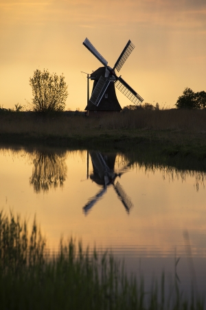 silhouette of a mill and its reflection in the water at sunriseの写真素材