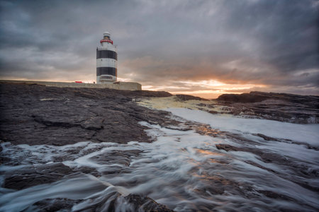 Hook Lighthouse, Wexford, Ireland. One of the oldest lighthouses in Europe still in operation. stones and very powerful waves in the foreground. Long exposure and silky water.の写真素材