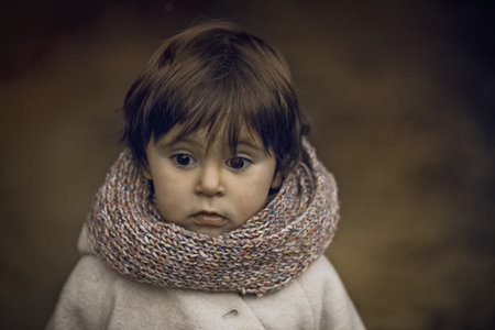 Adorable 4 year old girl with scarf. An accurate portrait with an out of focus background and brown analogue tones. Very pretty expression on her face.の写真素材