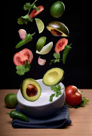 guacamole ingredients flying over bowl on black solid background. tomato, pepper, onion, garlic, avocado, coriander, limeの写真素材