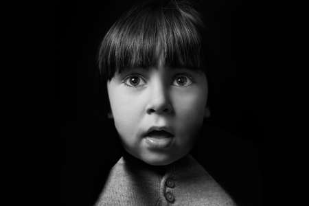 3 year old boy looking curiously at the camera. monochrome portrait on solid black background....