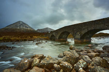 Dramatic sky over large mountains from the River Sligachan on the Isle of Skye Scotland with the Cuillin mountain range in the distance with snow in winter, Isle of Skye, Scotlandの写真素材