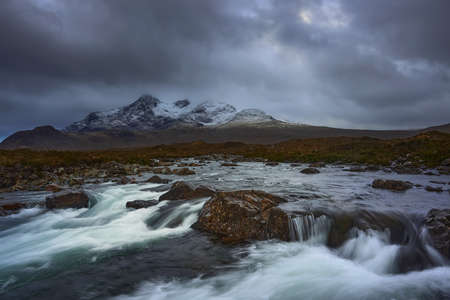 Dramatic sky over large mountains from the River Sligachan on the Isle of Skye Scotland with the Cuillin mountain range in the distance with snow in winter, Isle of Skye, Scotlandの写真素材