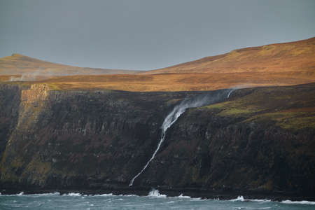 waterfall on cliff in windy day with spray of water going back towards the mountain. Scotland, Isle...