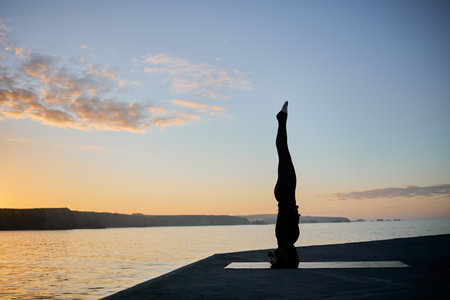 woman practicing a difficult yoga pose during sunset timeの写真素材
