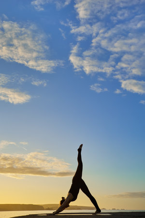 attractive woman silhouette doing a yoga pose in a sunrise with cloudy skyの写真素材