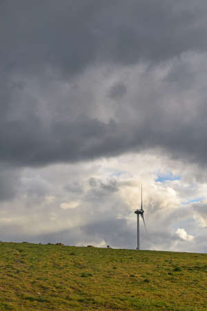 wind energy tubin on top of a hill with large cloudy sky copy space