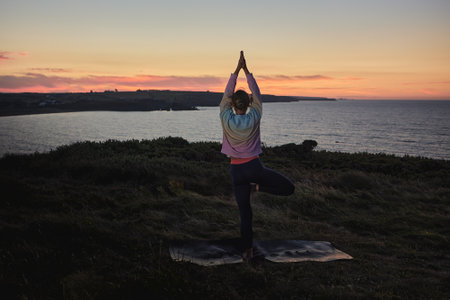 attractive woman practicing yoga at sunrise in front of the ocean.の写真素材