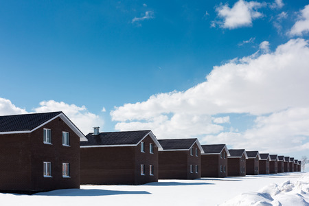 the same dark houses in the sun. The sky is blue with clouds. Snow covered earth. Minimalism.の写真素材