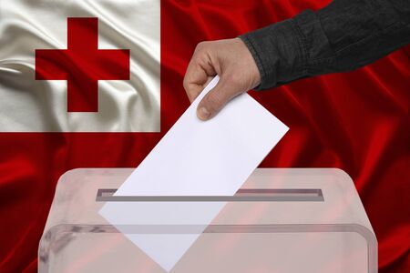 male voter drops a ballot in a transparent ballot box on the background of the Tonga national flag, concept of state elections, referendumの写真素材
