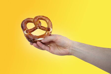 beautiful freshly baked pretzel, German national dish with a golden brown crust in a male hand close-up, the concept of traditional Hesse cuisine, organic foodの写真素材
