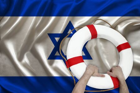 male hands hold on a white lifebuoy against the background of the silk national flag of the country of Israel, the concept of medical insurance, tourism, disaster, humanitarian assistanceの写真素材