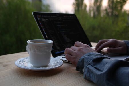 man, businessman, programmer, working in the evening at a laptop on the balcony of his house, hands closeup, concept of remote work, quarantine, downshiftingの写真素材