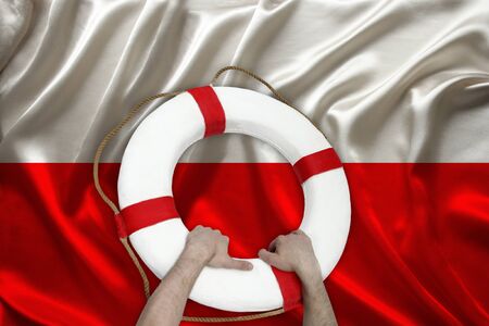 male hands hold on a white lifebuoy against the background of the silk national flag of Poland, the concept of medical insurance, tourism, disaster, humanitarian aidの写真素材