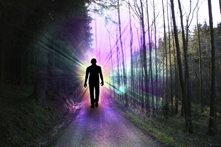 black silhouette of a man with luminous rays of energy in a dark forest on the road among the trees, the concept of aura, living energy, death and the transition to another worldの写真素材