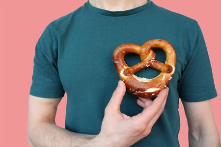 beautiful freshly baked pretzel, heart, German national dish with a golden brown crust in a male hand close-up, the concept of traditional Hesse cuisine, organic foodの写真素材