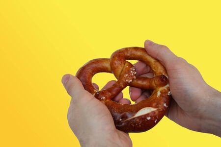 beautiful freshly baked pretzel, German national dish with a golden brown crust in a male hand close-up, the concept of traditional Hesse cuisine, organic foodの写真素材