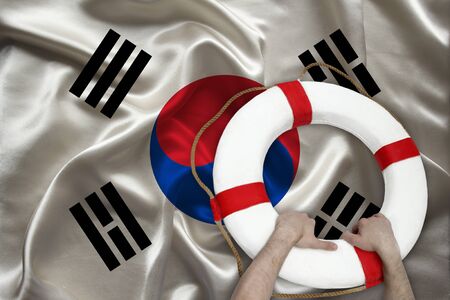 male hands hold on a white life buoy against the backdrop of the silk national flag of the country of South korea, the concept of medical insurance, tourism, disaster, humanitarian assistanceの写真素材