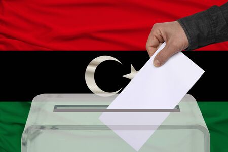 male voter drops a ballot in a transparent ballot box against the background of the Libya national flag, concept of state elections, referendumの写真素材