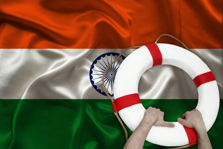 male hands hold on a white lifebuoy against the background of the silk national flag of india...