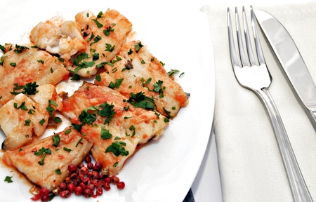 Cod dish with bits of parsley on top and red peppercorns on one sideの写真素材