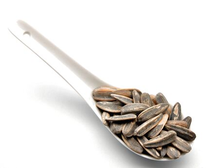Sunflower seeds stacked next to each other, in a spoon surrounded by white backgroundの写真素材
