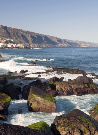 View of a beach with waves in the Spanish town of Puerto de La Cruz, are some rocks in the sea, and the mountain in the backgroundの写真素材