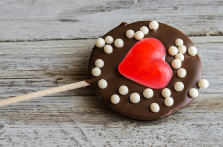 Close-up of delicious chocolate lollipop with red jelly in shape of heart in wooden tableの写真素材