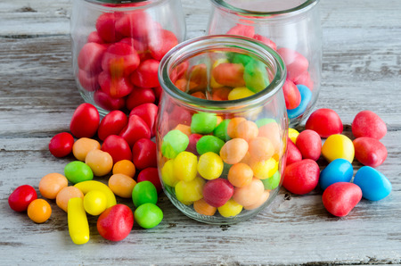 Close-up of colorful bright candies in glass jars and scattered on tableの写真素材