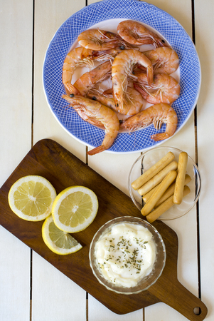 Close up of cooked shrimps in blue plate with slices of lemon and breadsticks with sauce on wooden deskの写真素材