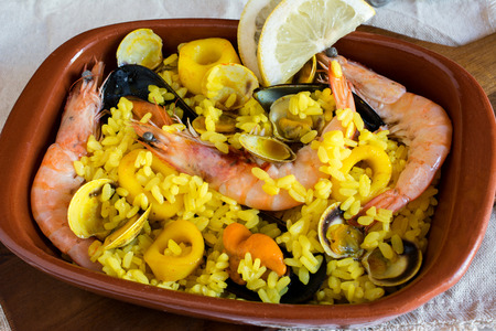 Close up of cooked shrimps with yellow rice and vegetables and oisters with slices of lemon in brown plateの写真素材