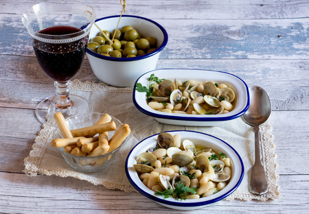 Still life of delicious oyster soup with bread sticks,olives and glass of red wine on napkin