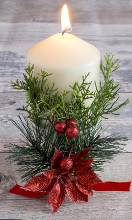 Still life of white burning candle tied with green plant and holly flower on wooden background.の写真素材