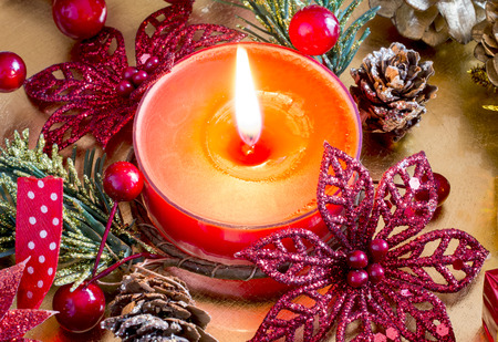 Cloe-up of burning red candle with Christmas decorations.の写真素材