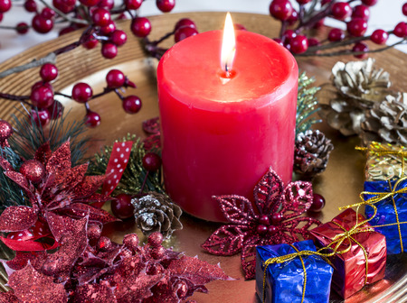 Close-up of bright burning candle on golden plate with Christmas decorations.の写真素材