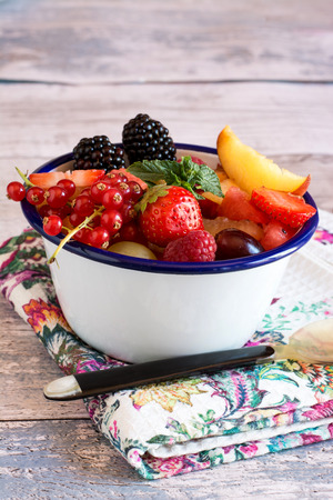White bowl with blue rim full of delicious raspberry,strawberry,peach,grape,cranberry with mint leafの写真素材