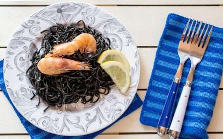 Close up of meal with coocked shrimps and black seaweed served with slices of lemon. Pair of forks lying on blue napkinの写真素材